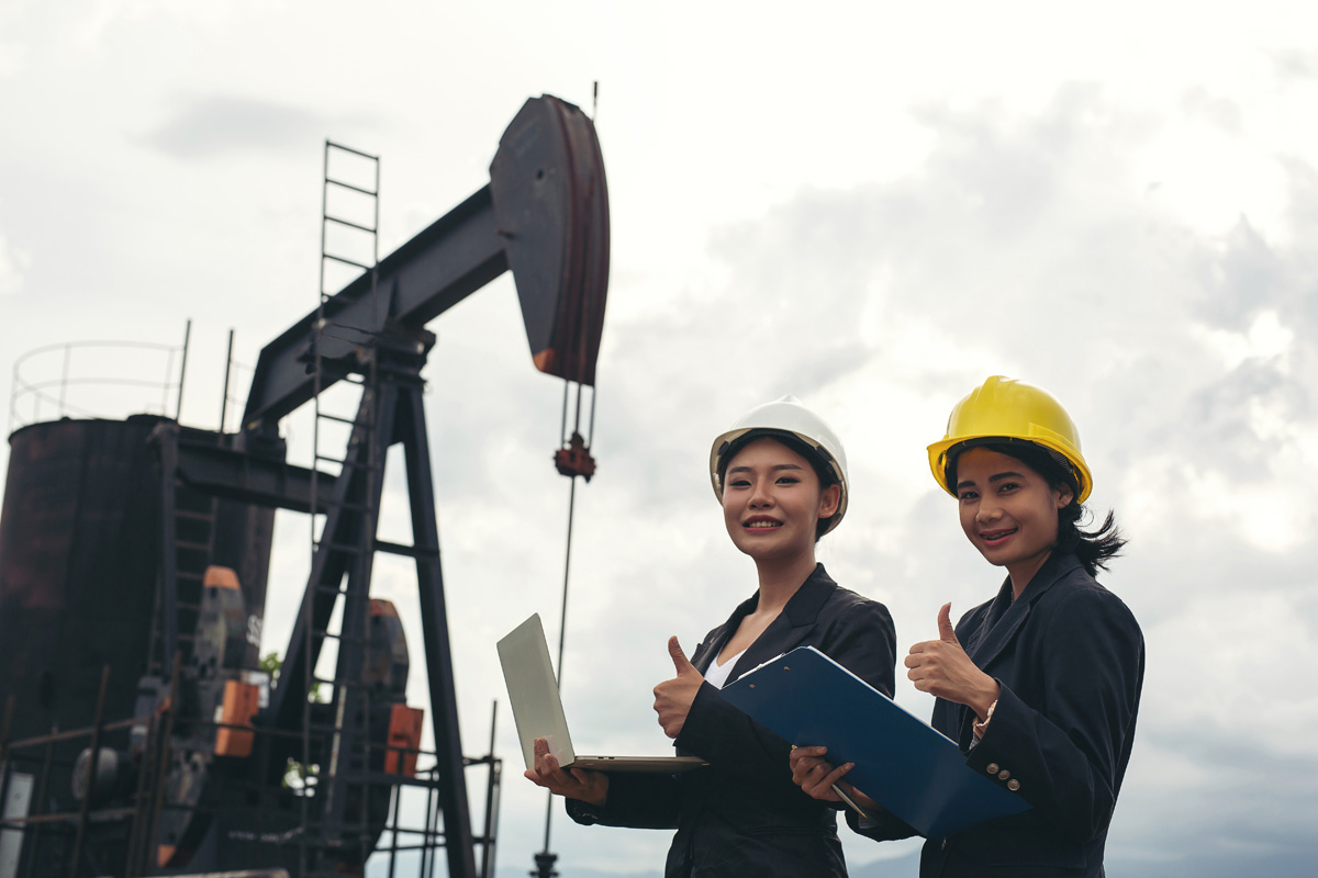 Two female engineers stand beside working oil pumps with a white